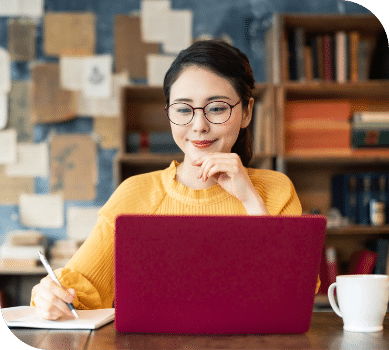 A woman takes notes on a notepad while working on a computer.