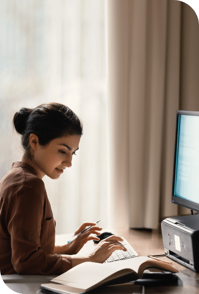 A woman works at a computer while referencing printed material